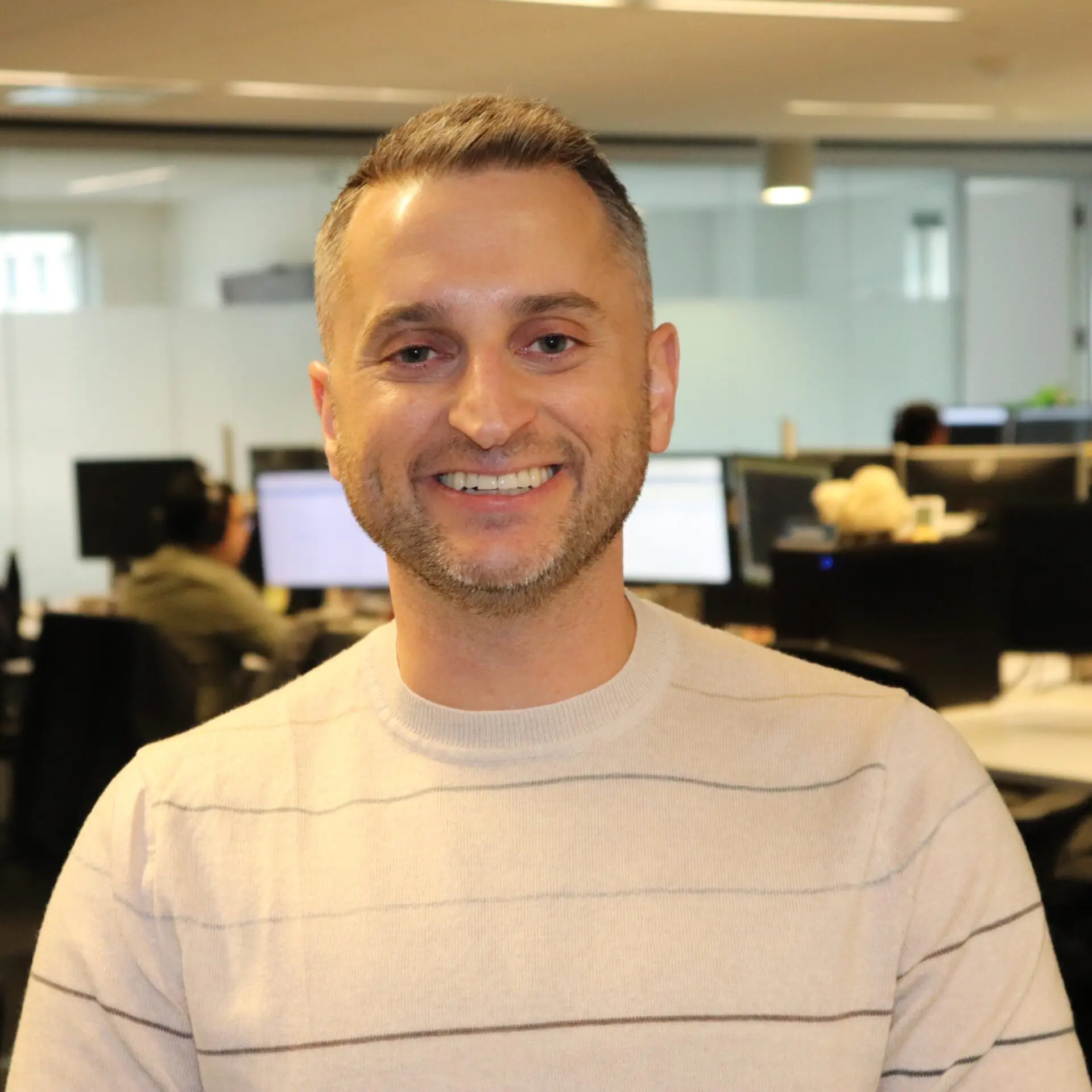 Smiling man in beige sweater standing in modern open-plan office